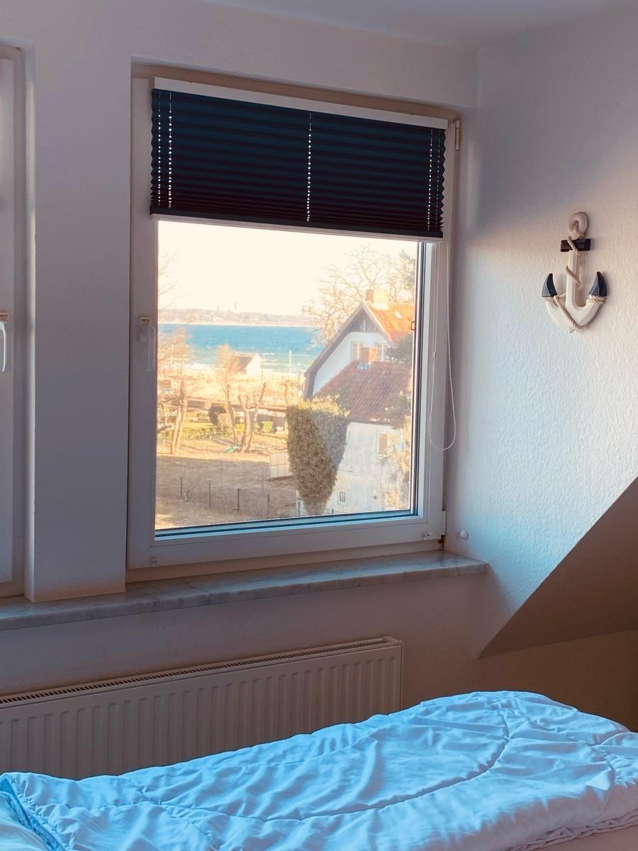 A bed with blue bedding in front of a window with sea view and a white anchor on the wall.