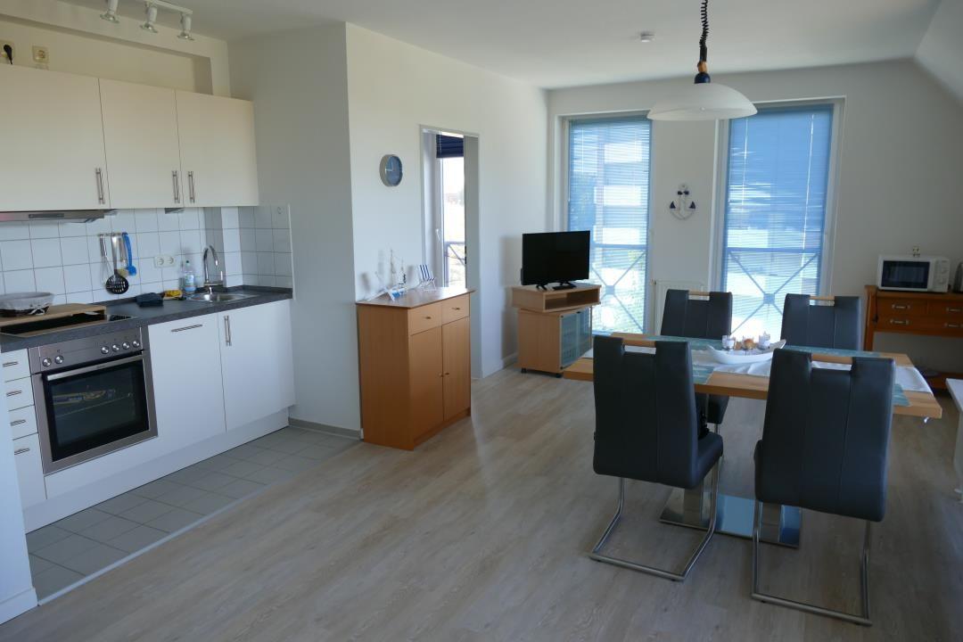Kitchen with dining area and TV. Wooden floor and large windows.