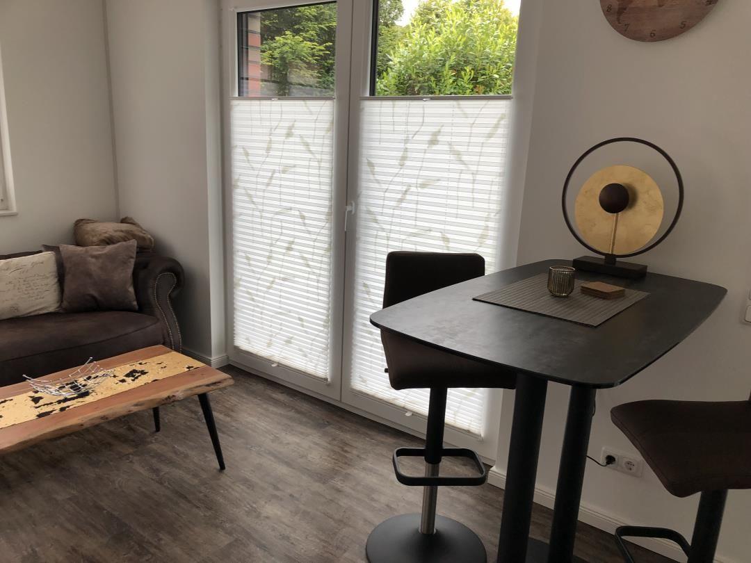 Ein Raum mit Sofa, Tisch und Stühlen vor einer Glastür mit Jalousien.