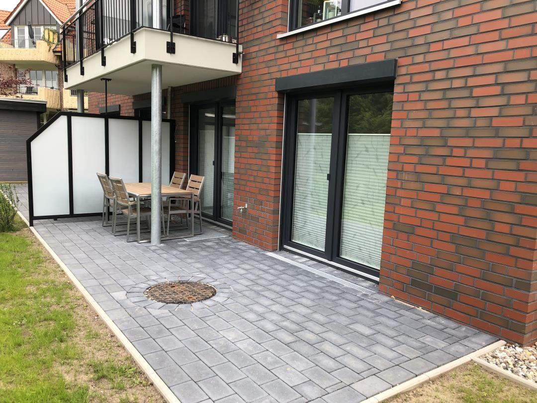 Terrasse mit Tisch und Stühlen neben rotem Backsteinhaus mit Glasfronten.
