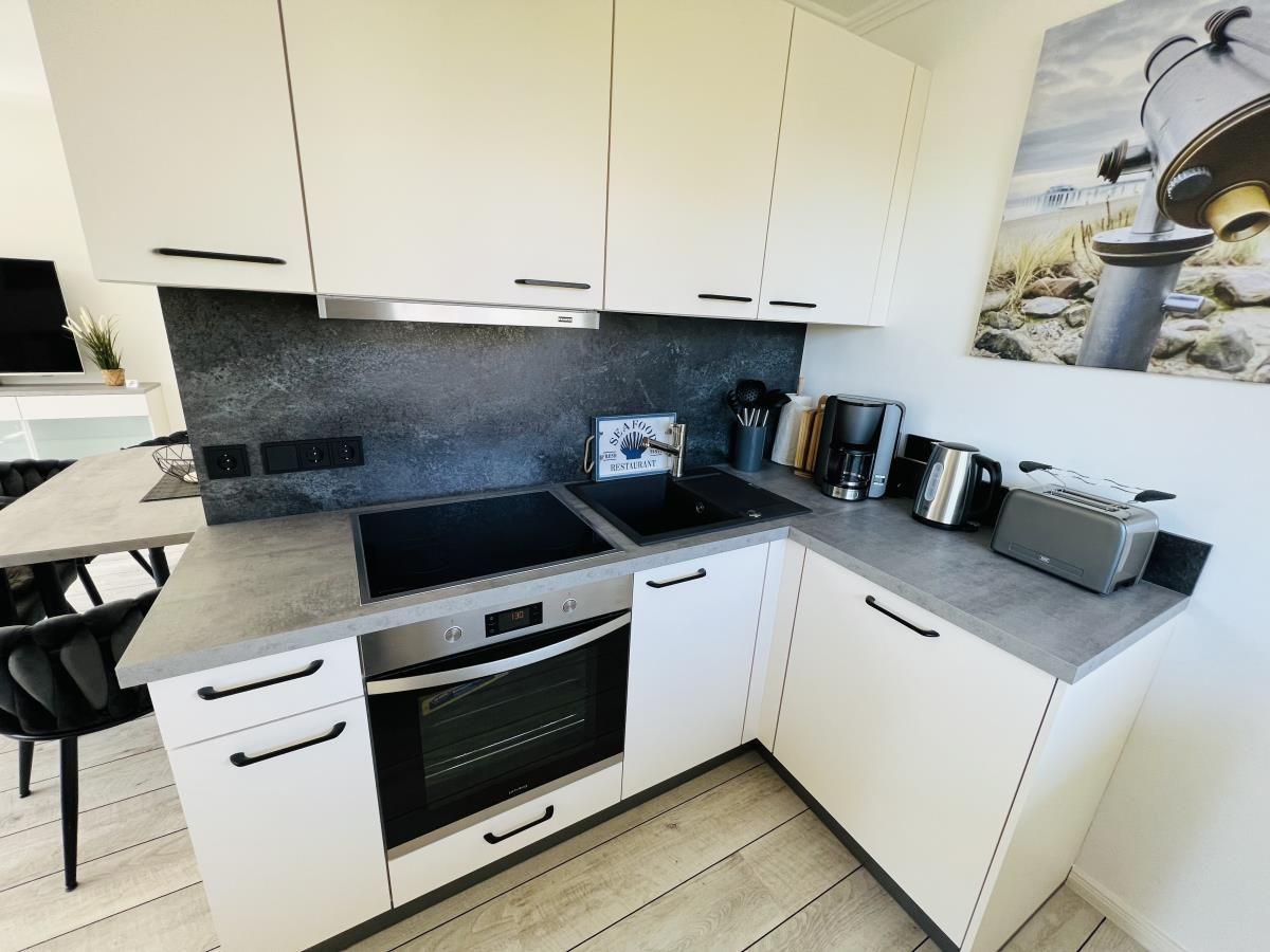 Kitchen with white cabinets, induction cooktop, and oven. A picture hangs on the wall.