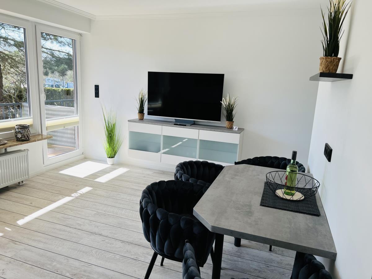 Living and dining area with TV, table and chairs. Windows to the terrace.