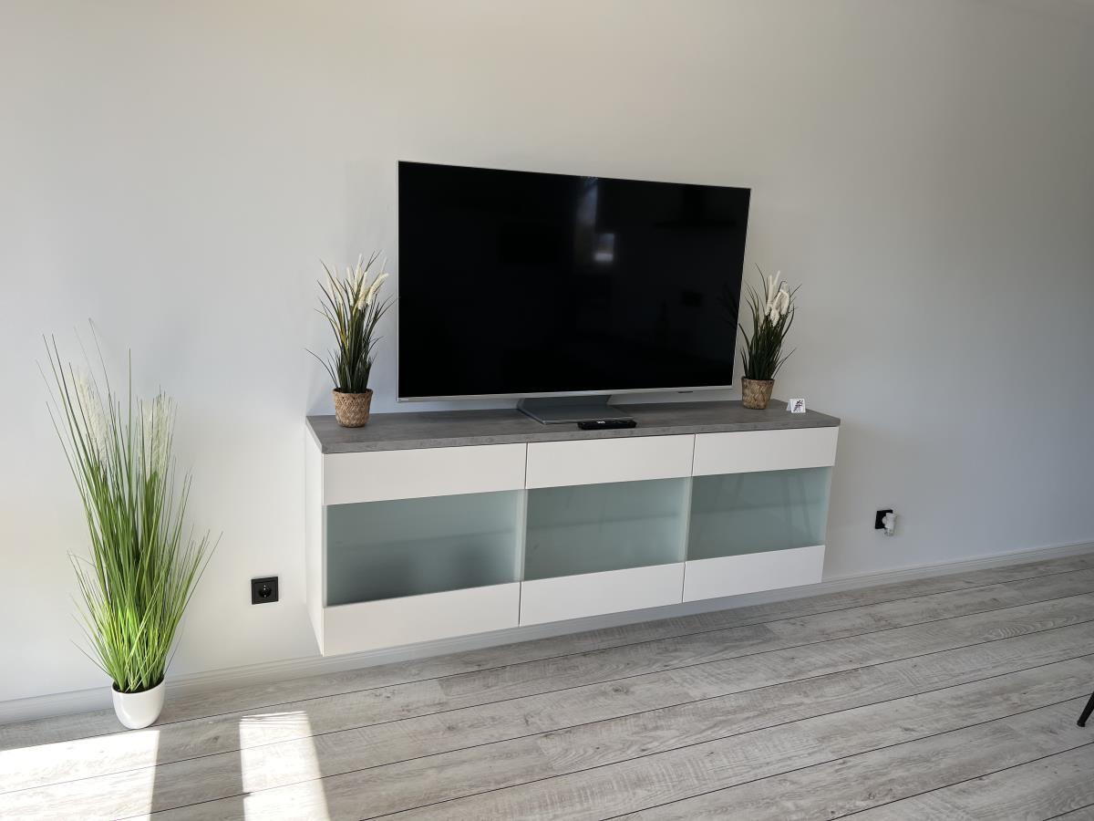 Flat-screen TV on modern cabinet with glass fronts and plants.