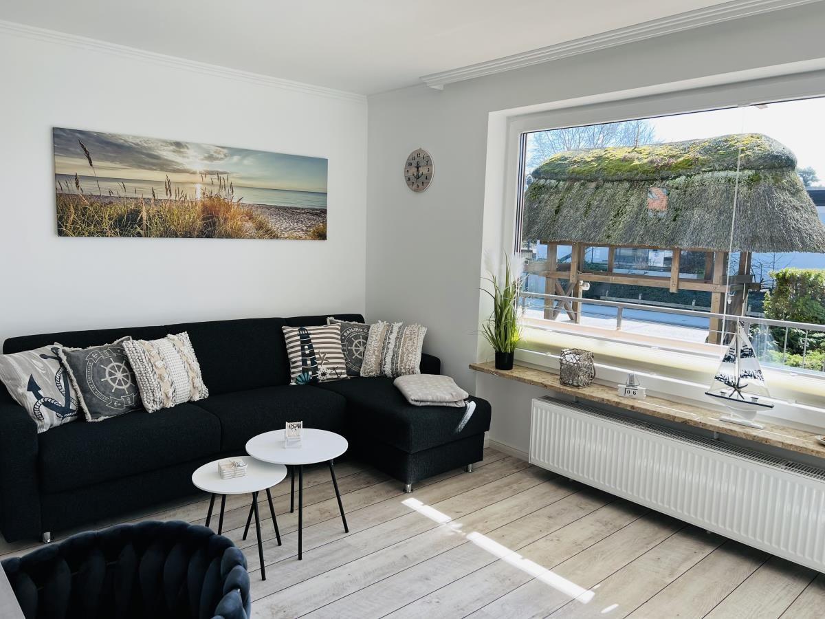 Living room with black sofa, view of thatched roof through window