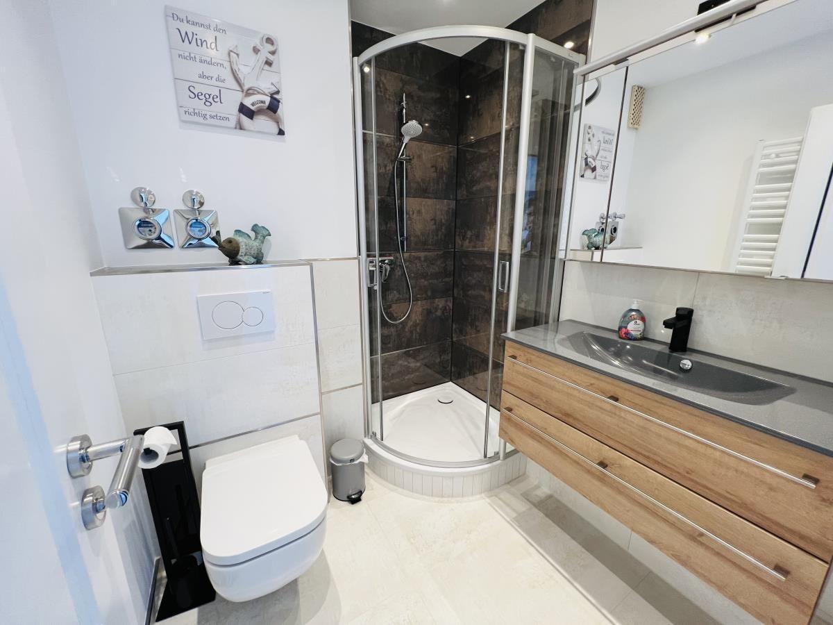 Bathroom with shower, sink, and toilet. Wall decor and mirror visible.