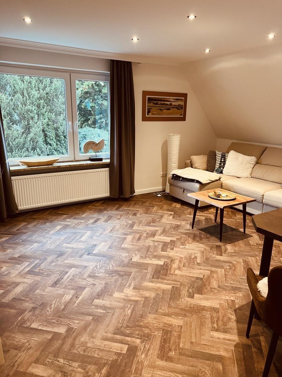 Wohnzimmer mit Holzboden, Sofa und Fenster mit Blick auf Bäume