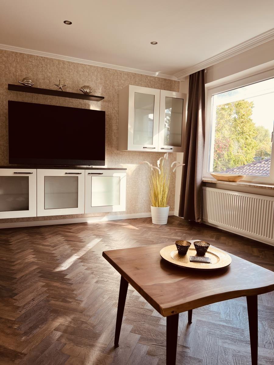 Wohnzimmer mit TV, Holzboden und Fensterblick auf Grün.