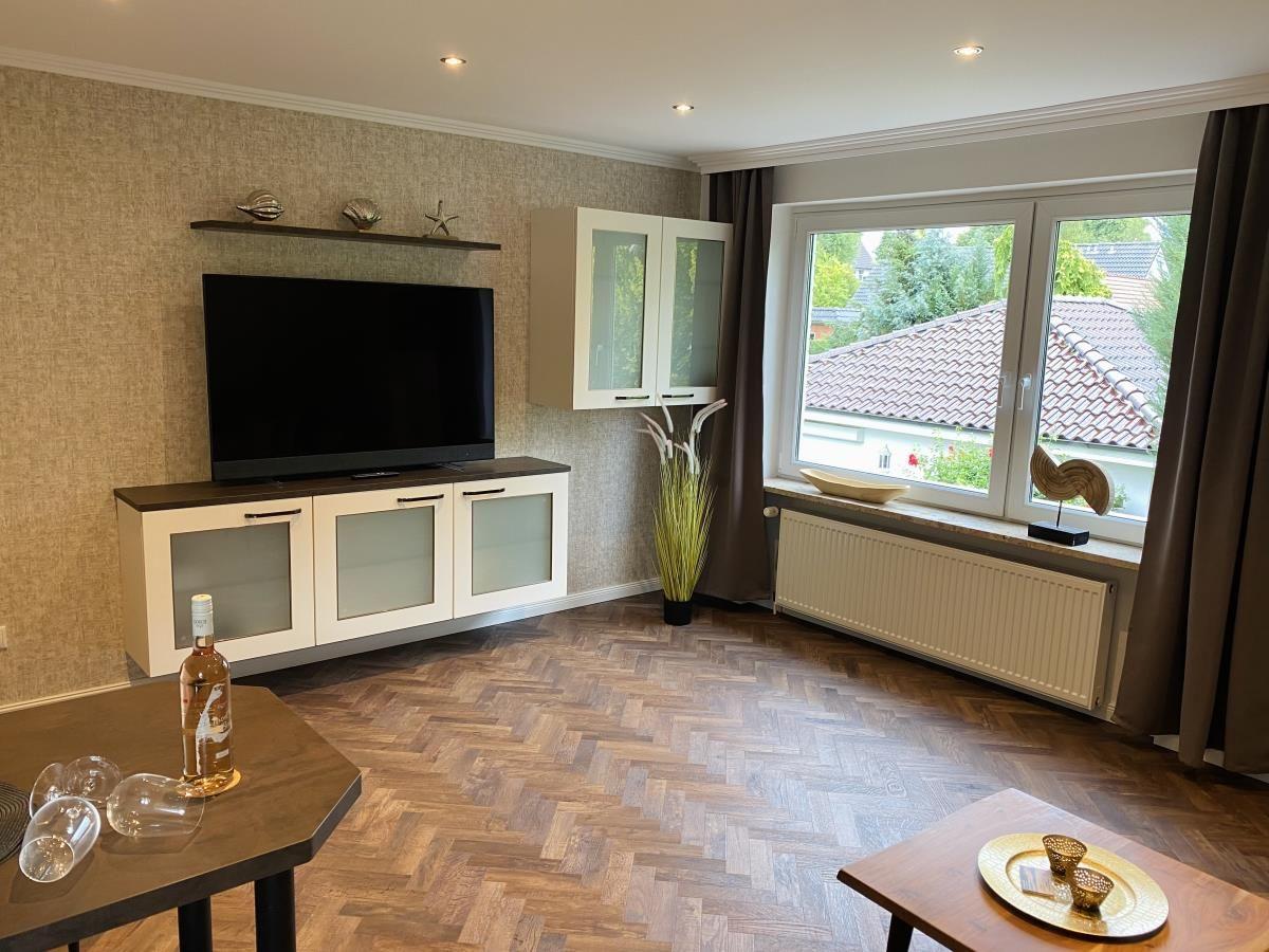 Wohnzimmer mit TV, Holzboden und Fenster mit Blick auf Dächer.