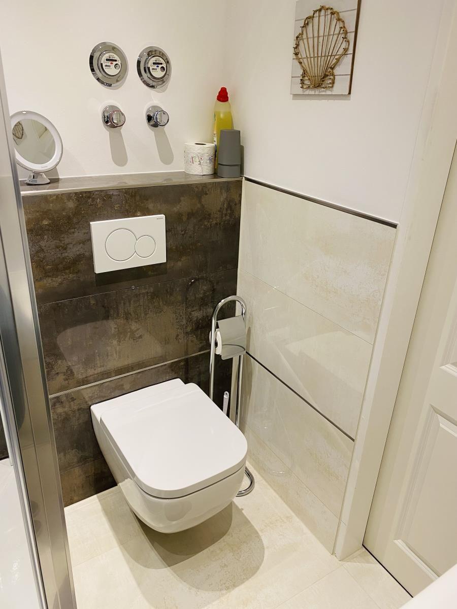 Hochwertige Toilette mit modernem Wandspülkasten und dekorativen Wandkacheln.