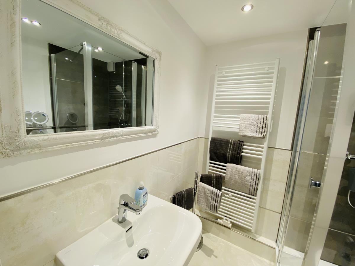 Badezimmer mit Waschbecken, Spiegel, Dusche und Handtuchhalter.