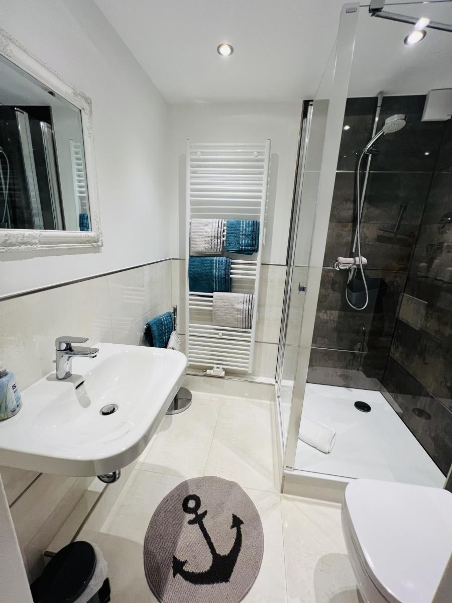 Badezimmer mit Dusche, Waschbecken und Heizkörper mit Handtüchern.