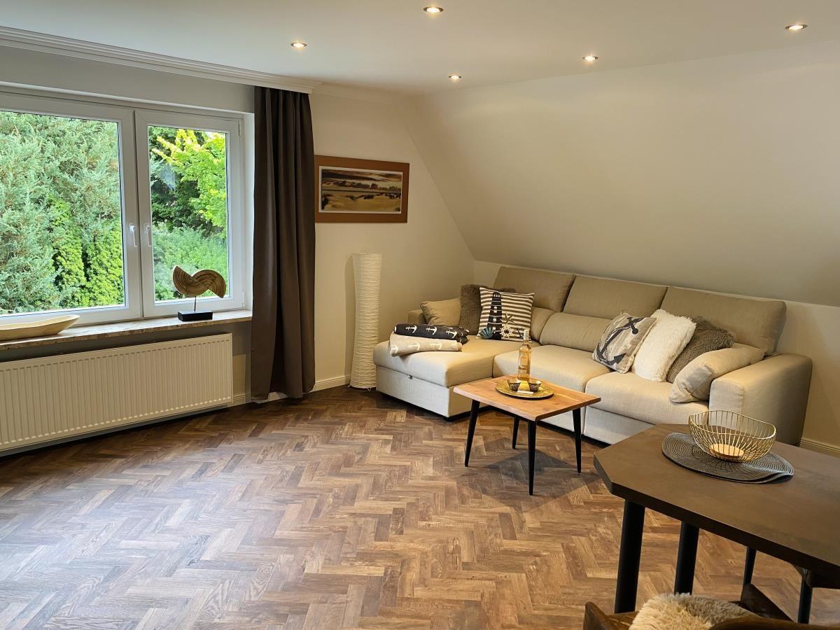 Wohnzimmer mit Sofa, Holzboden und großem Fenster mit Blick auf Grün.