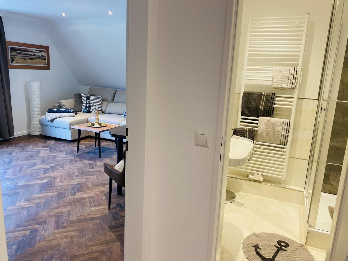 Wohnzimmer mit Sofa und Holzboden. Nebenbei Bad mit Heizkörper und Dusche.