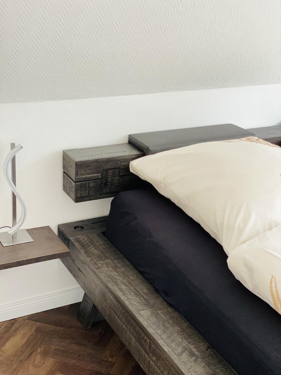 Schlafzimmer mit Holzbett, Wandlampe und Holzboden.