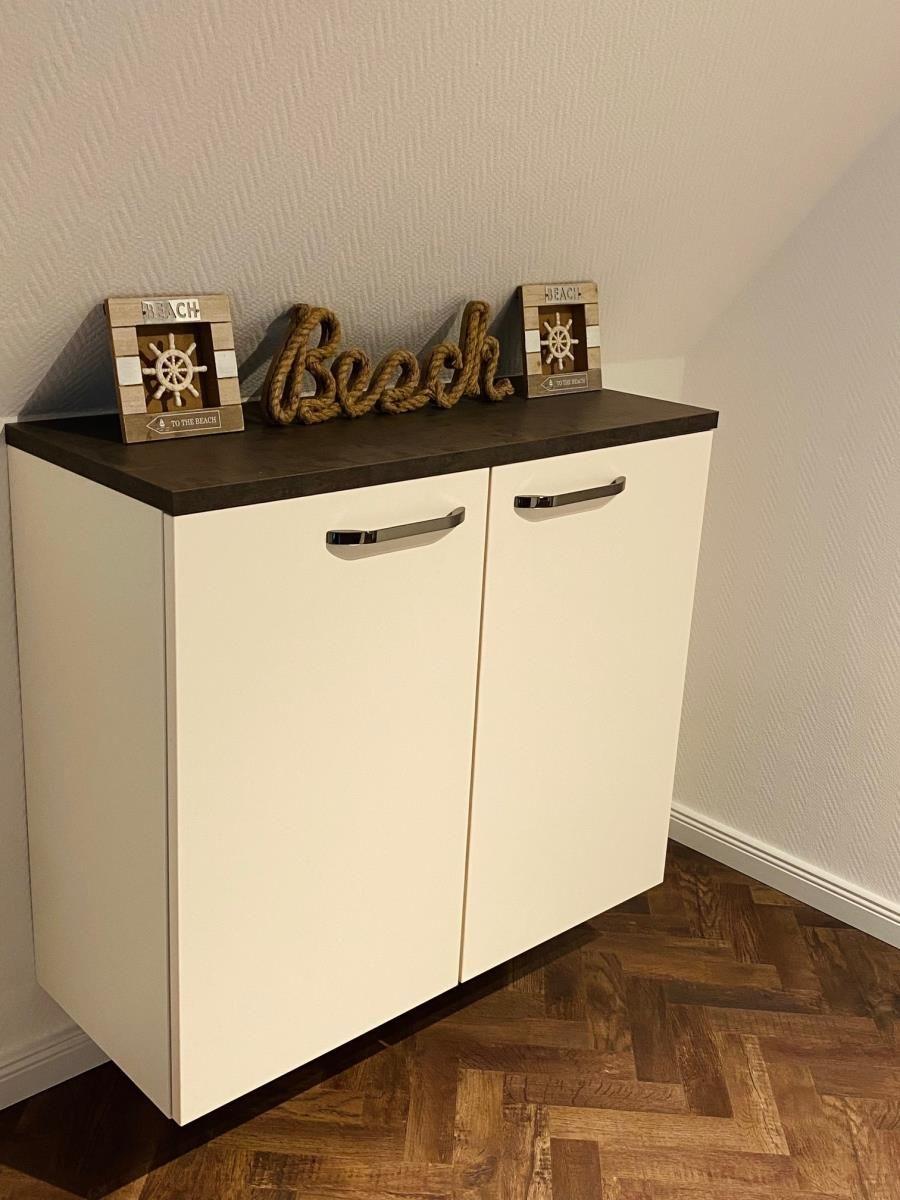 Weißer Schrank mit dunkler Arbeitsplatte und Seil-Schriftzug. Hintergrund Wand und Holzboden.