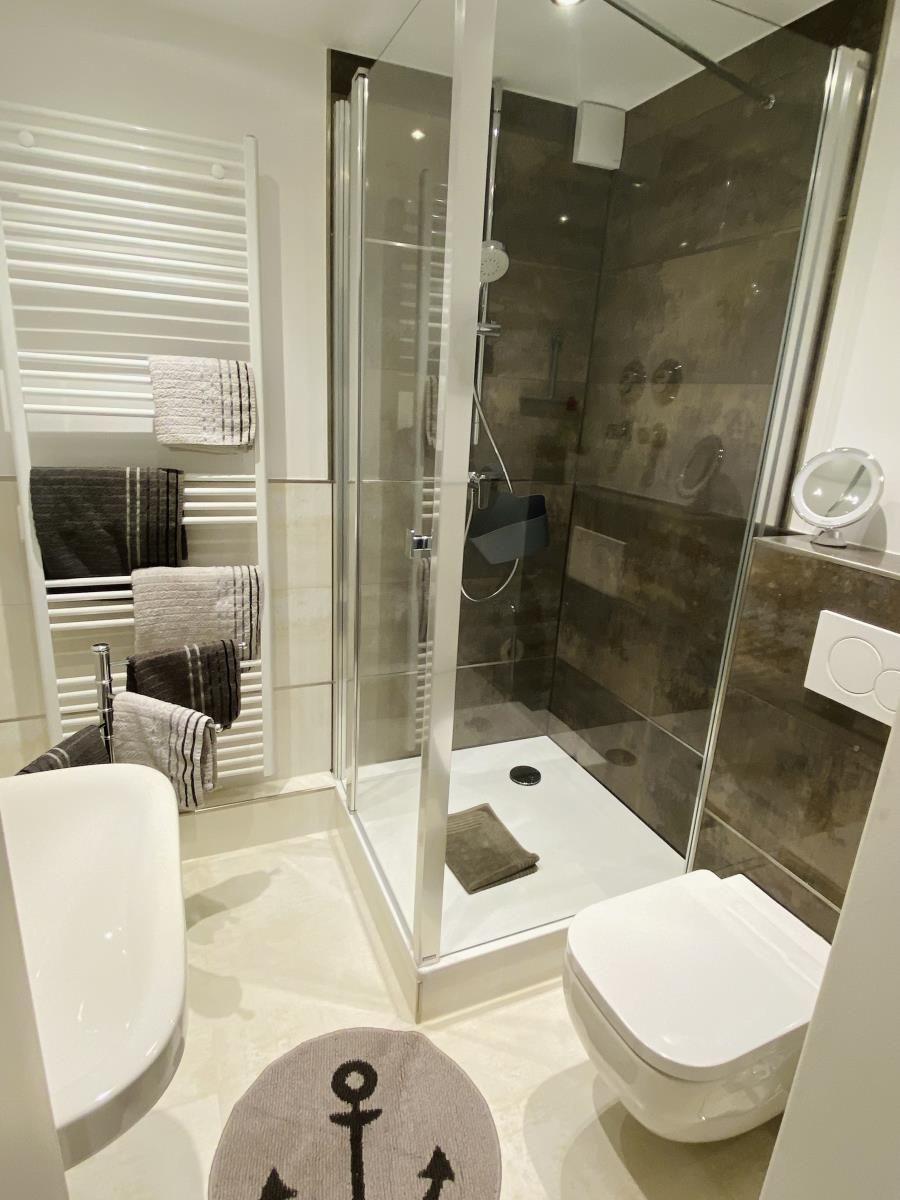 Badezimmer mit Dusche, Toilette und Heizung. Handtuchhalter und Bodenmatte mit Anker.