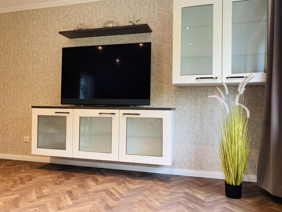 Wohnzimmer mit Fernseher, Schrank und Pflanze auf Holzboden.