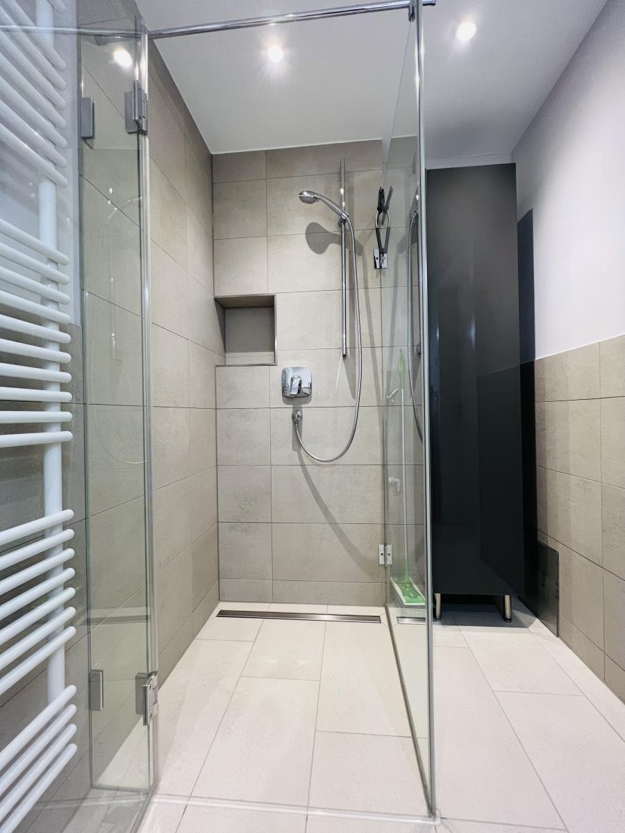 Dusche mit Glaswand, Duschbrause und Heizkörper an der Wand