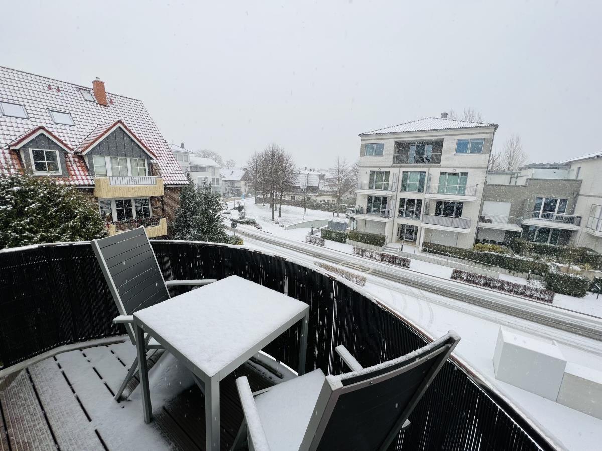 Balkon mit Tisch und Stühlen im Schnee. Blick auf Wohnhäuser und verschneite Straße.
