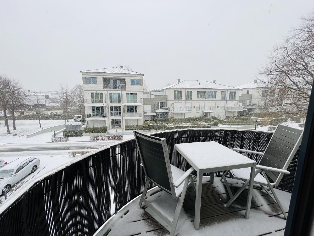Terrasse mit Tisch und zwei Stühlen, bedeckt mit Schnee, Blick auf Wohnhäuser.