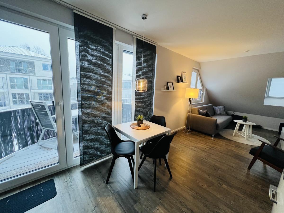 Wohnung mit Essbereich, Sofa und Balkon. Holzboden und große Fenster.