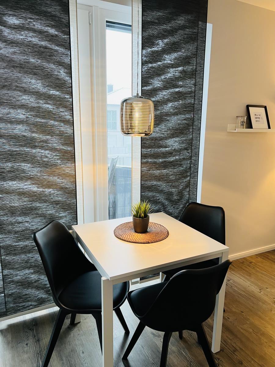 Ein Essbereich mit weißem Tisch, drei schwarzen Stühlen und einer Pflanze auf dem Tisch.