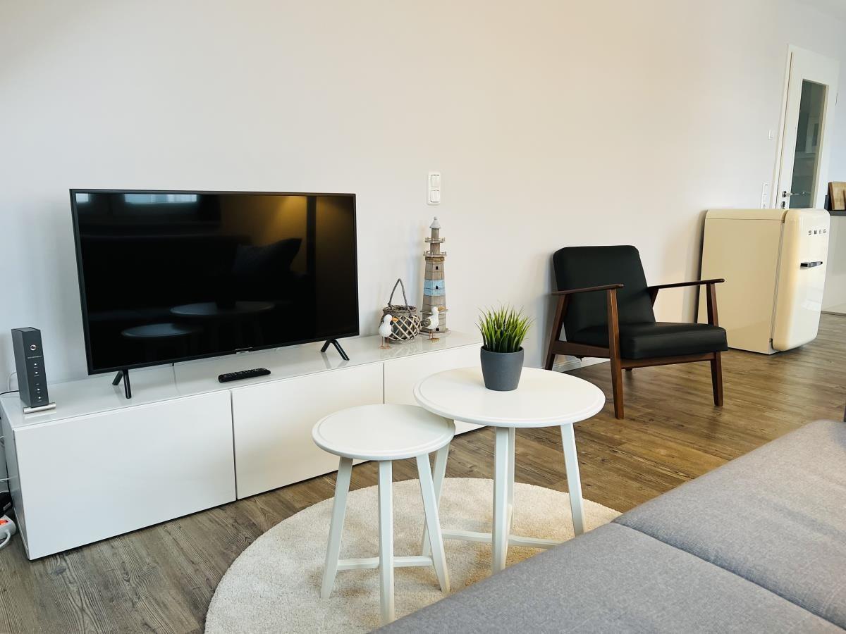 Wohnzimmer mit Fernseher, Sitzgruppe und Kühlgerät.