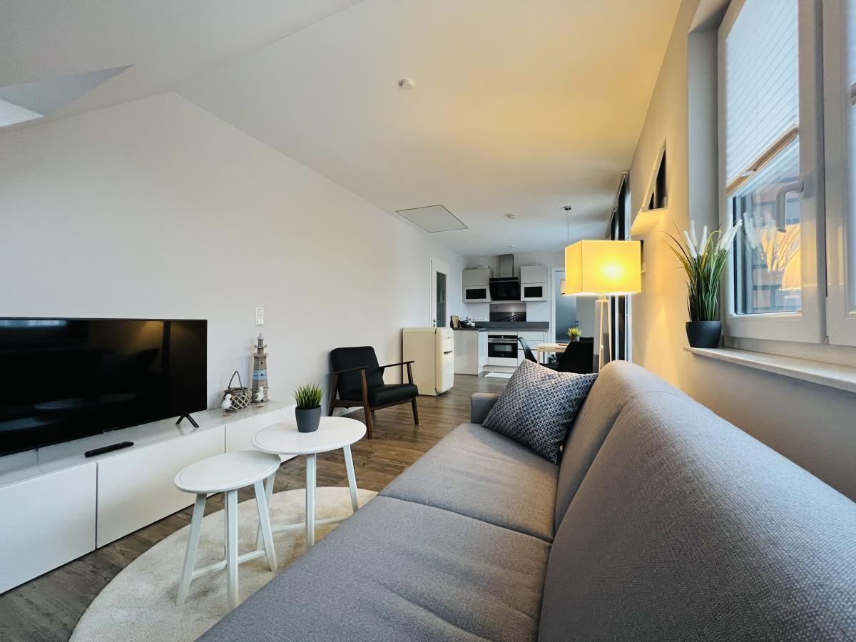 Wohnzimmer mit Sofa, Fernseher und Küchenbereich im Hintergrund.