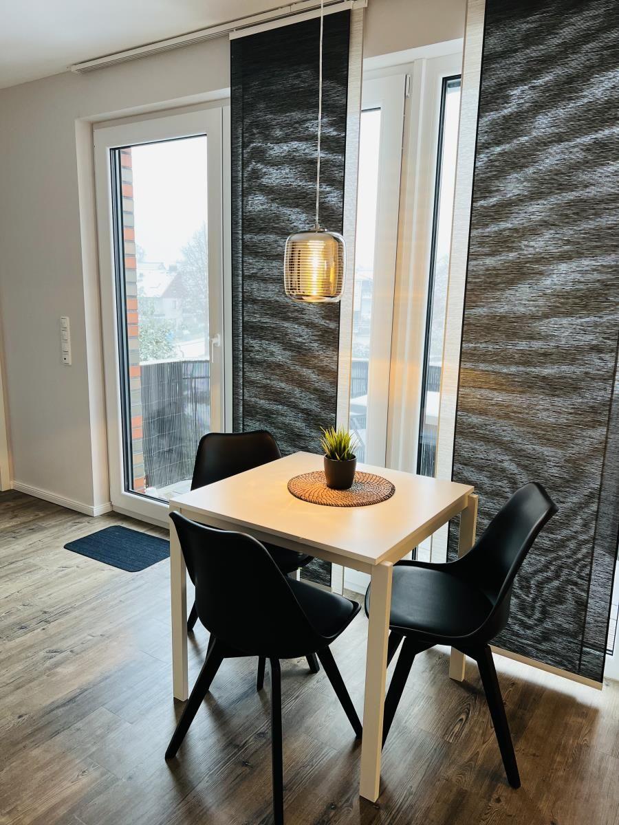 Esstisch mit vier Stühlen vor großem Fenster mit Blick auf Balkon.