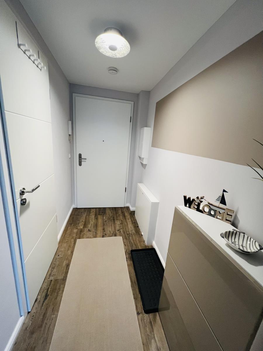 Flur mit Holzboden, Schuhregal, Willkommensdekoration und Tür.