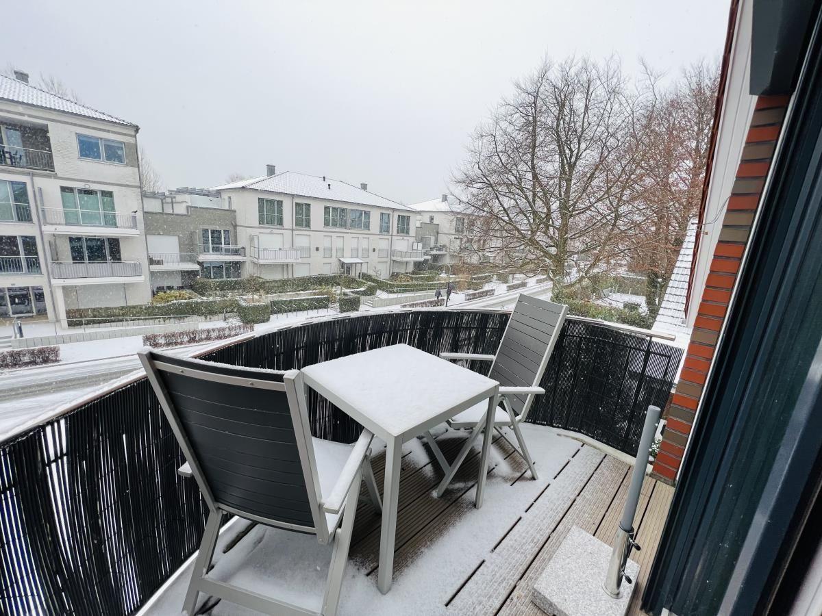 Terrasse mit Tisch und zwei Stühlen, bedeckt mit Schnee. Blick auf Wohnhäuser und Bäume.