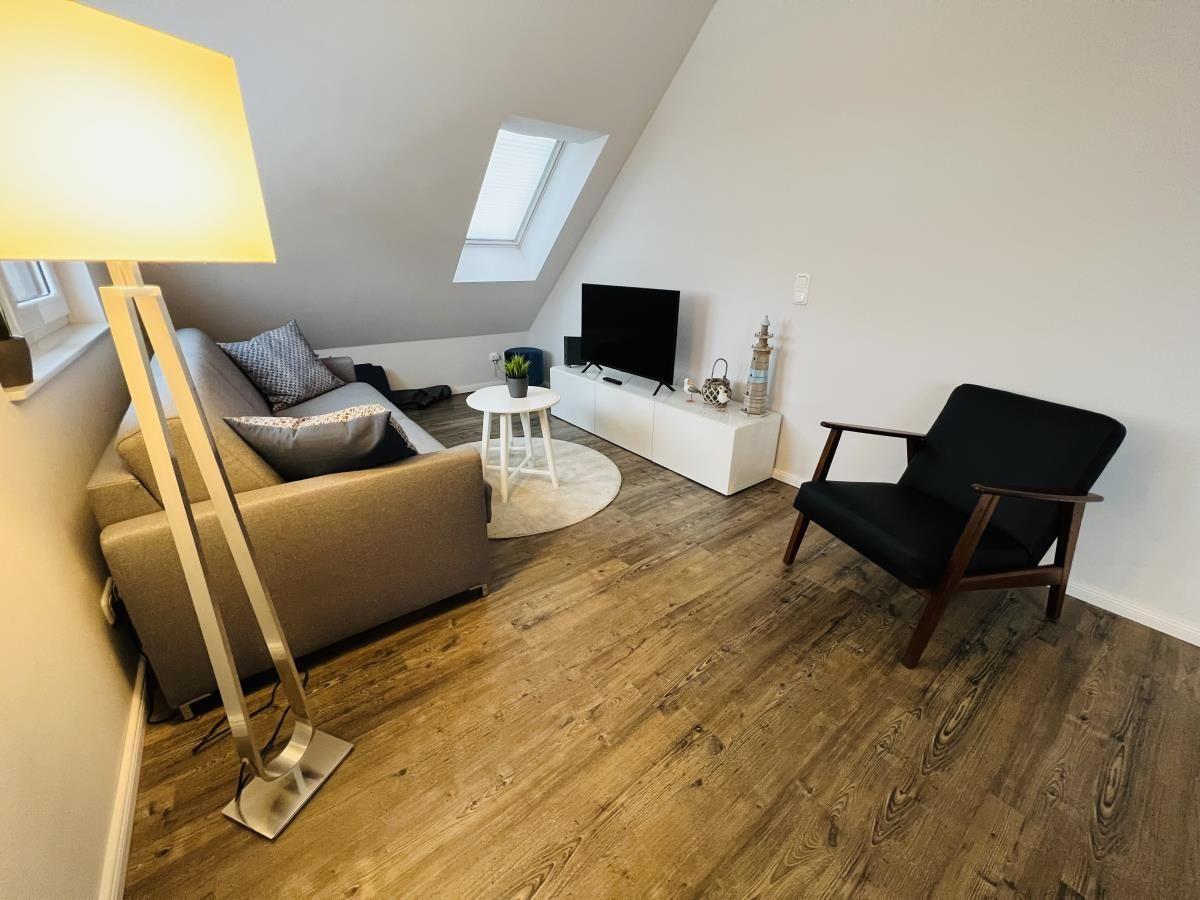 Wohnzimmer mit Sofa, Sessel, Fernseher und Holzboden