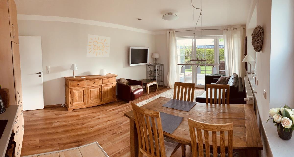 Living and dining area with wooden furniture and large window. Kitchen on the left.