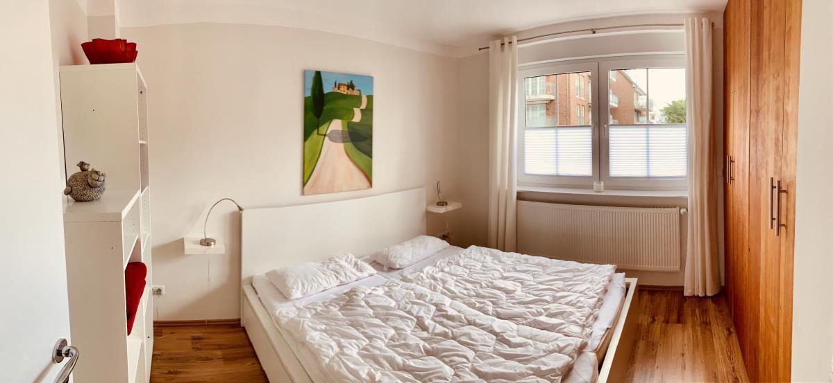 Bedroom with double bed, window, and wooden floor.