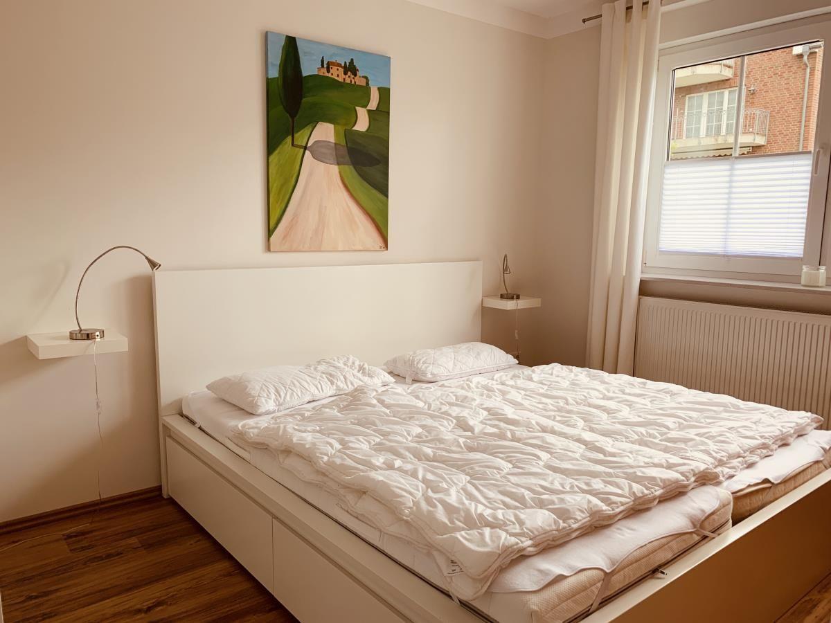 Bedroom with bed, wall painting, and window with blinds.