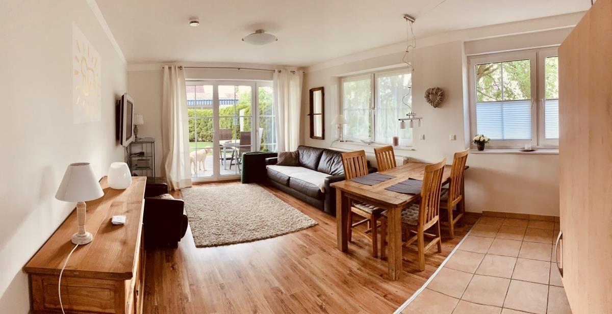 Living and dining area with wooden floor, sofa, dining table, and view to terrace.