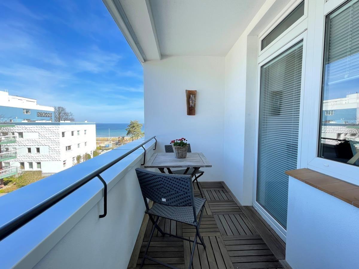 Balkon mit Tisch, Stühlen und Meerblick. Holzdecke und Fenster mit Jalousien.