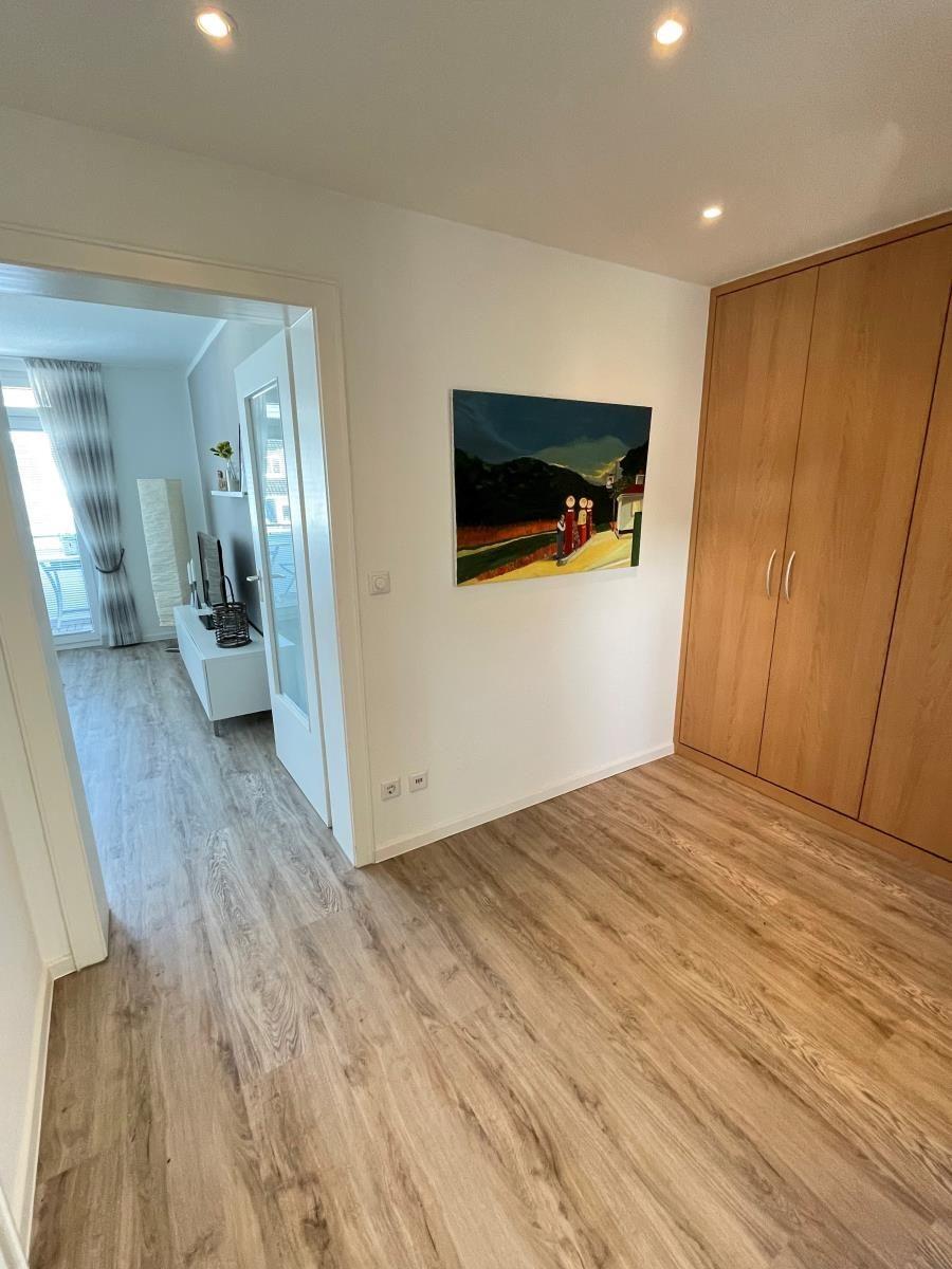 Schlafzimmer mit Holzboden, Kleiderschrank und Wandbild. Durchgang zur Wohnfläche.