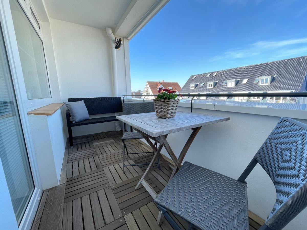 Terrasse mit Tisch, Stühlen und Pflanze. Blick auf Dächer und Himmel.