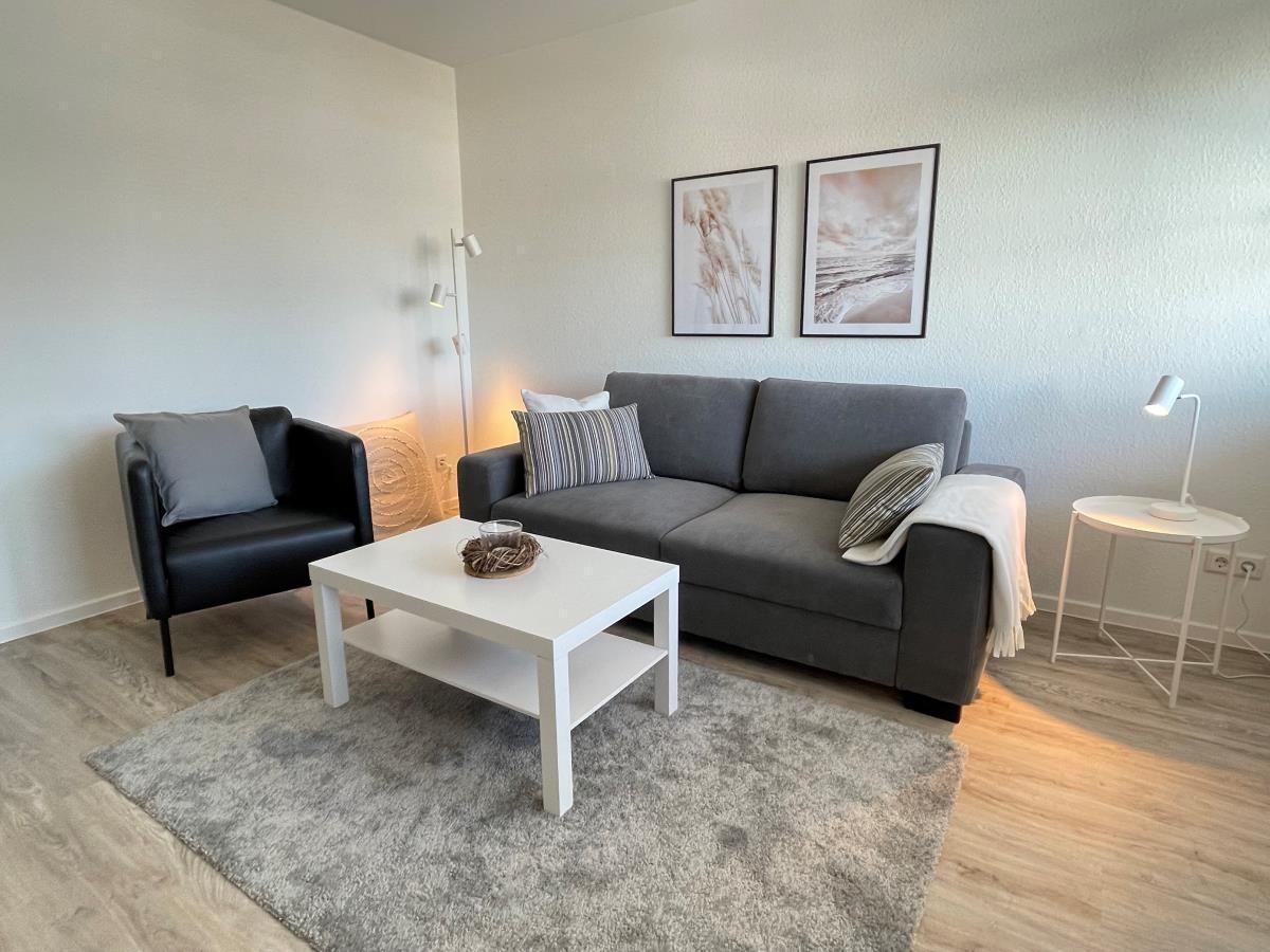 Wohnzimmer mit grauem Sofa, schwarzer Sitzgelegenheit und weißem Couchtisch.