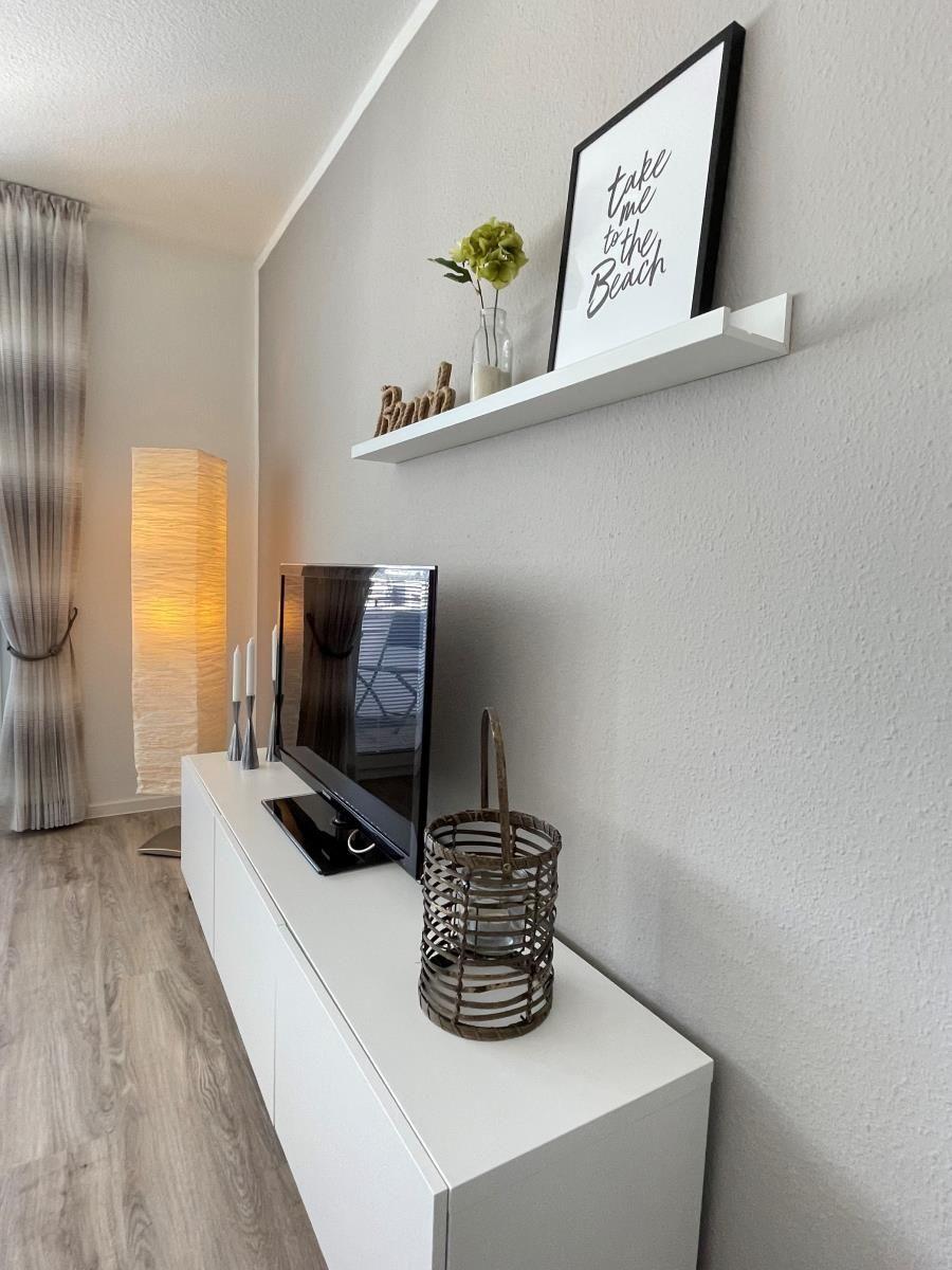 TV-Schrank mit Bild, Blumen und Korb. Hintergrund: Lampe und Vorhang.