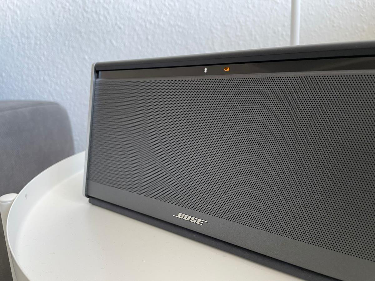 Bose-Lautsprecher auf runder Tischplatte mit grauer Sitzgelegenheit im Hintergrund.