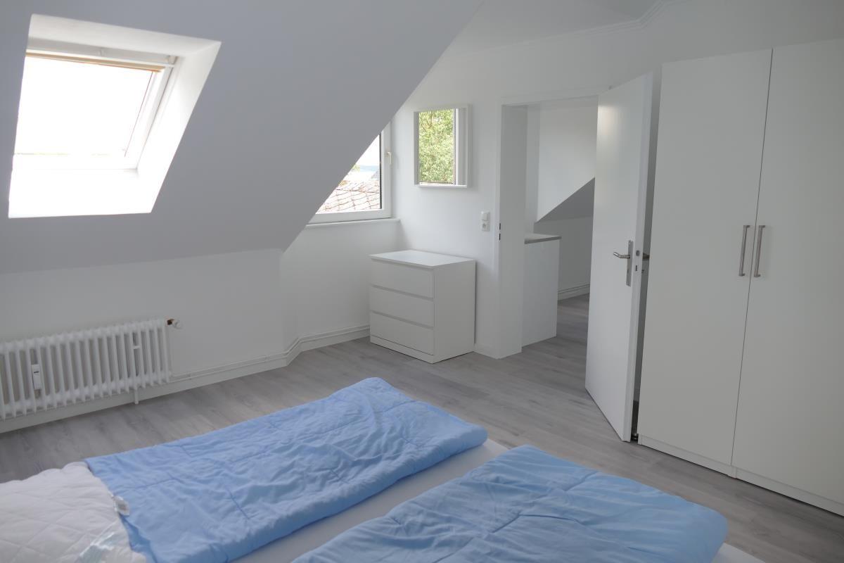 Schlafzimmer mit Dachschrägen, Fenster und weißem Schrank.