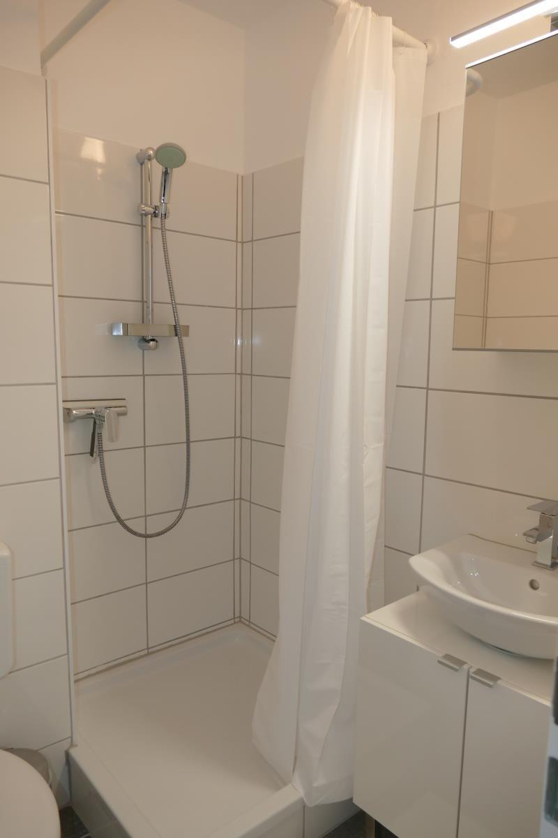 Badezimmer mit Dusche, Waschbecken und Spiegel.