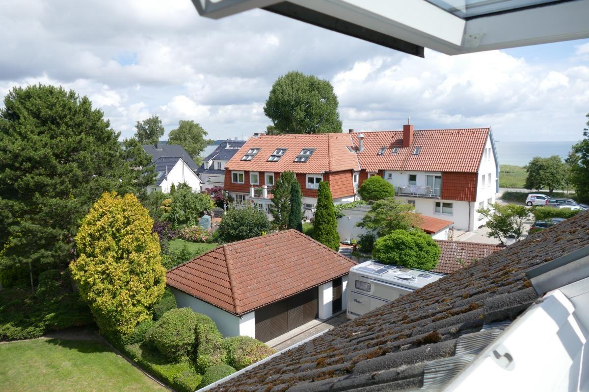 Panorama aus dem Dachfenster: Haus mit rotem Dach, Garten und Blick aufs Meer.