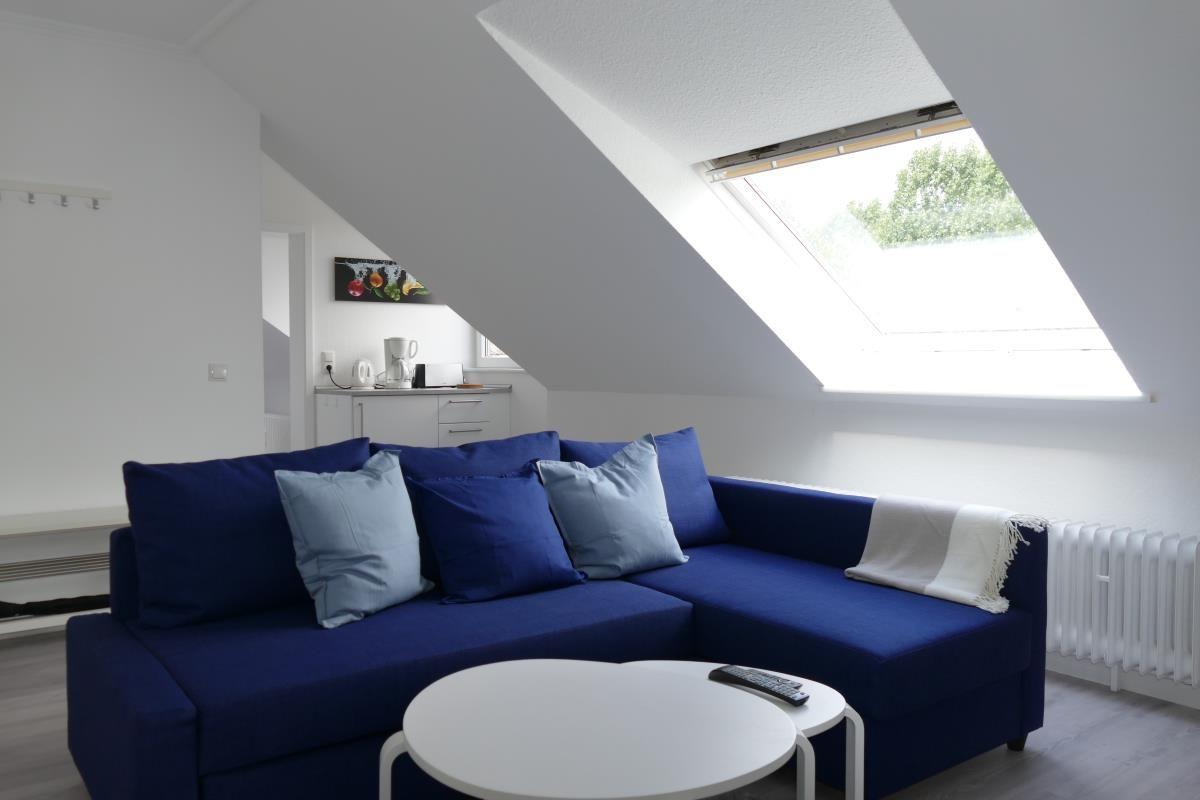 Ein Wohnzimmer mit blauem Sofa, runder Tisch und Dachfenster.