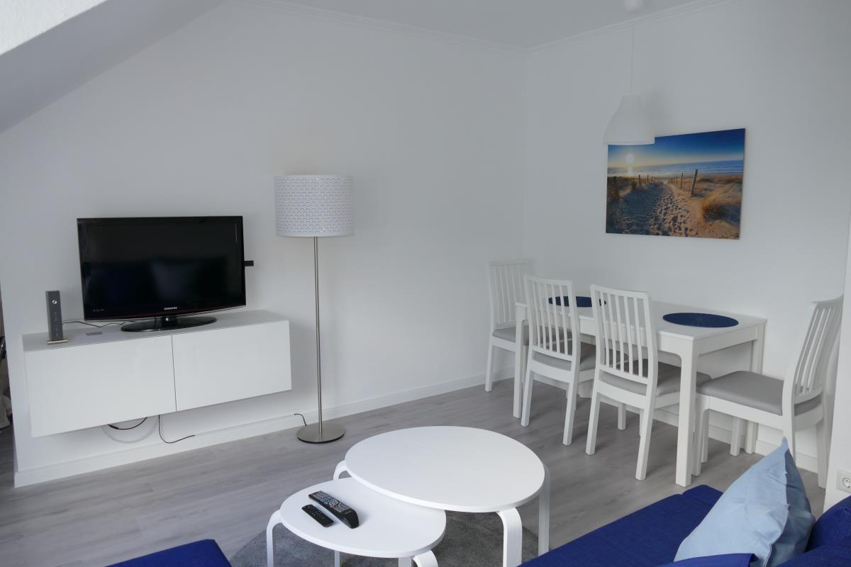Wohn- und Essbereich mit TV, Tisch, Stühlen und Wandbild.
