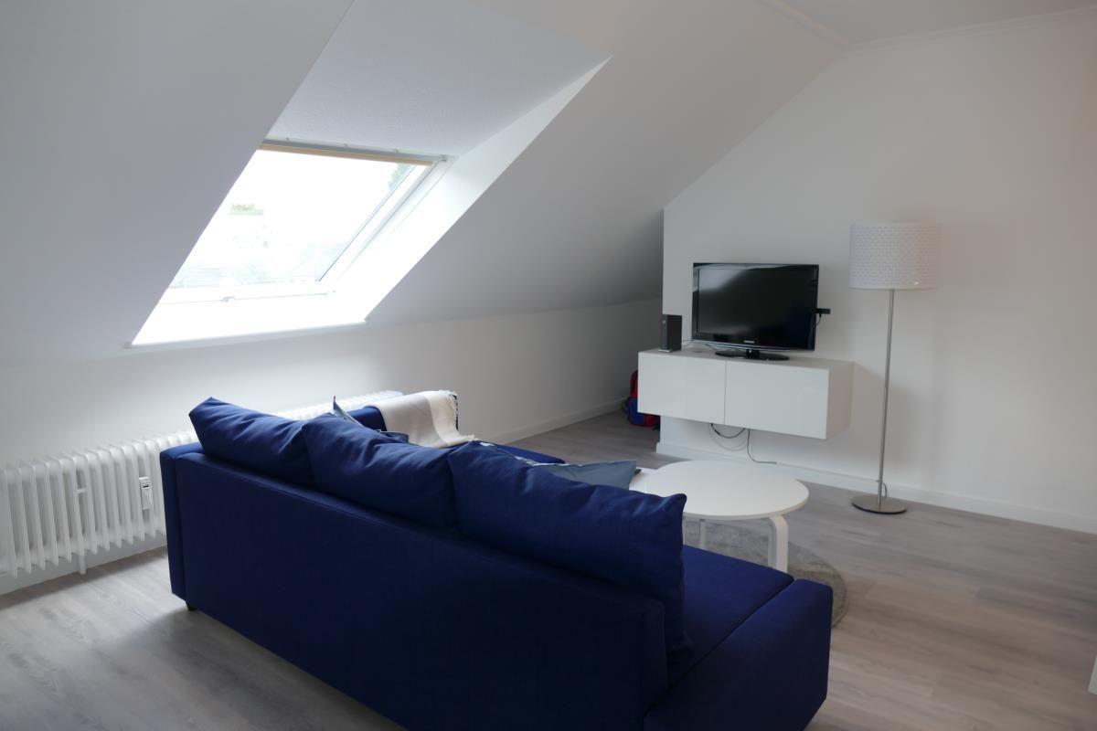 Wohnzimmer mit blauem Sofa, TV und Dachfenster.