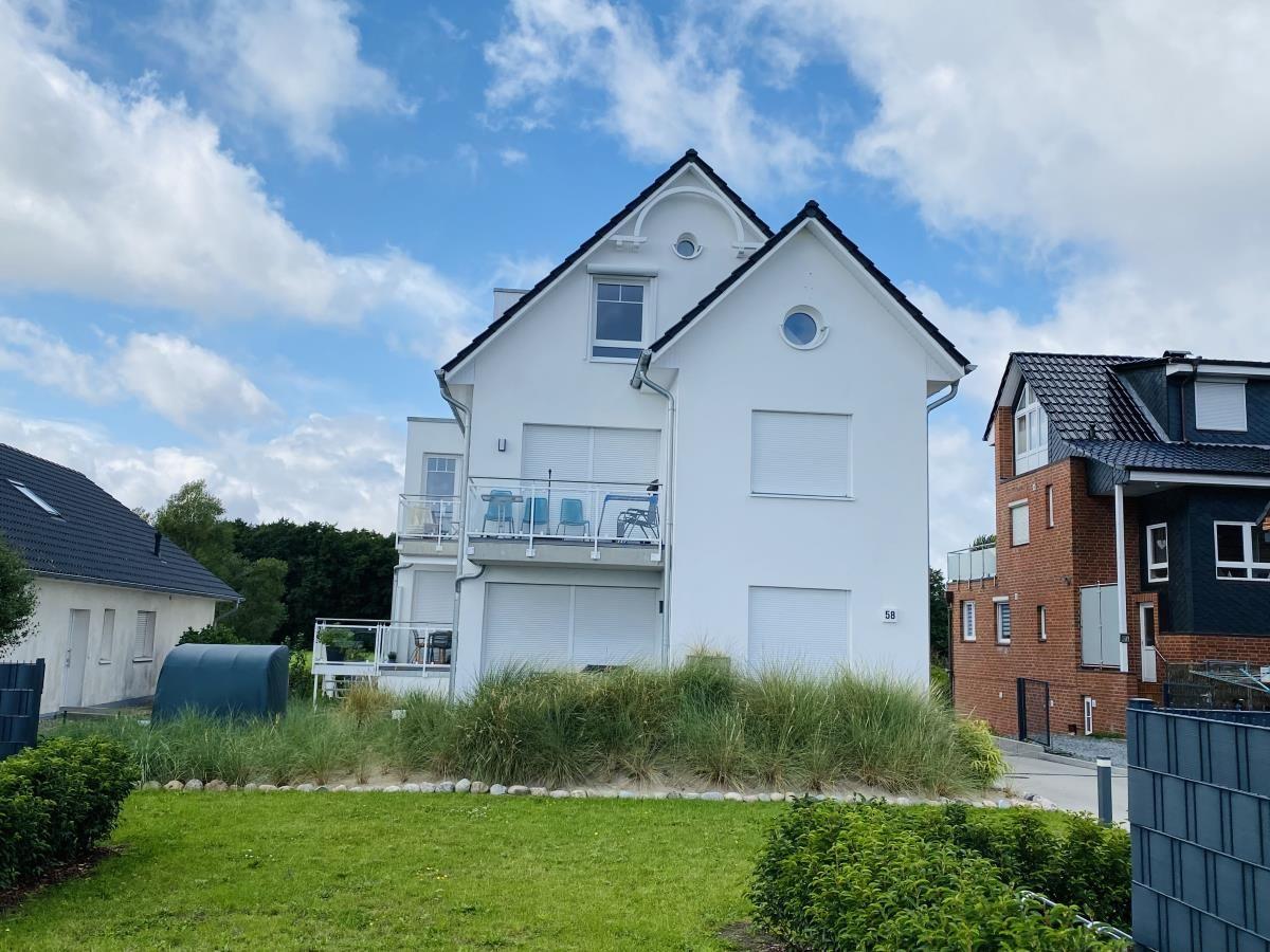 White house with balcony and garden. Background: other houses and blue sky.