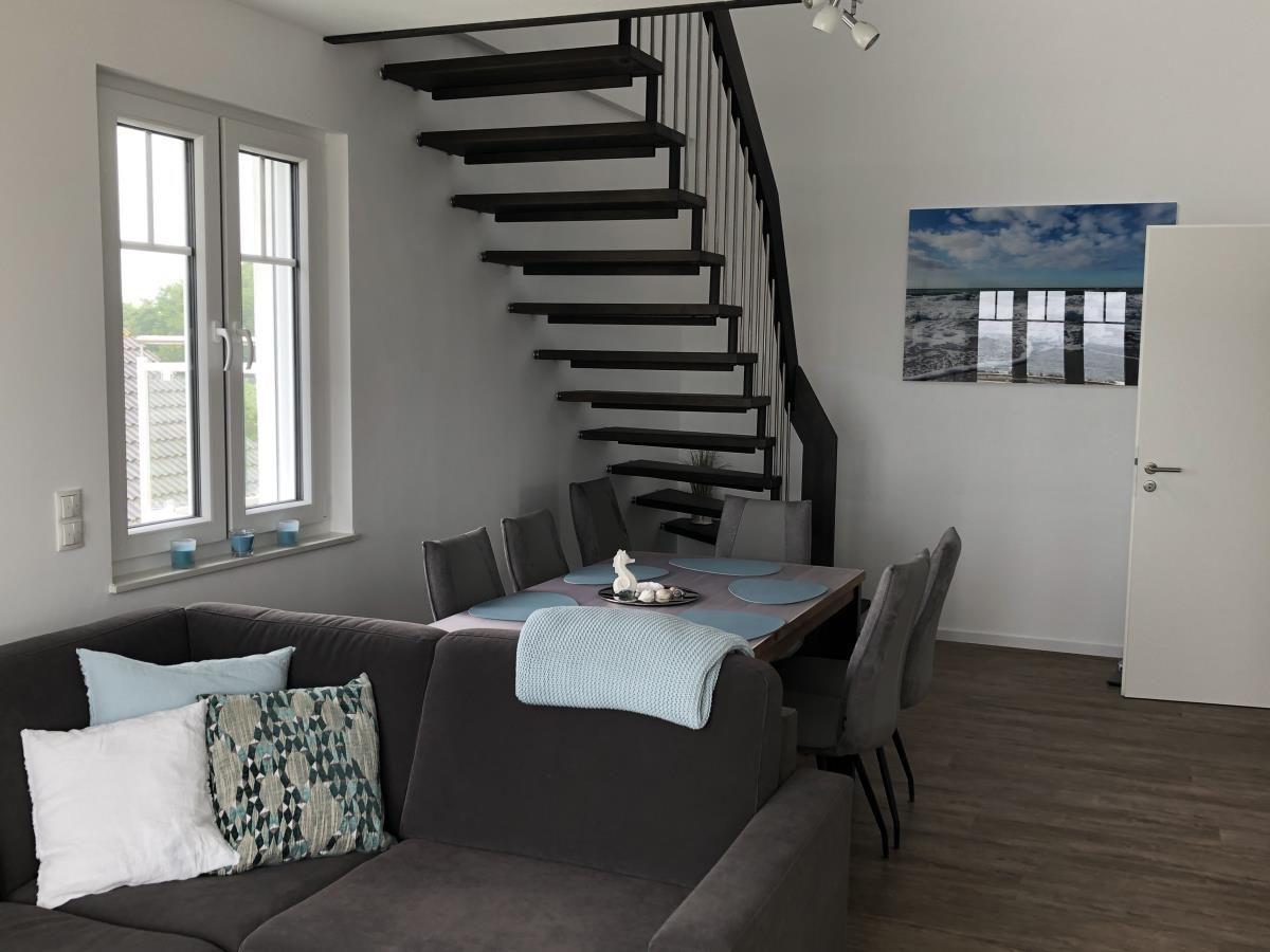 Living and dining area with staircase and window. Sofa, table, and chairs are visible.